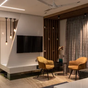 Apartment living room with a wall-mounted TV, two accent chairs, full-height curtains and a false ceiling with profile lights