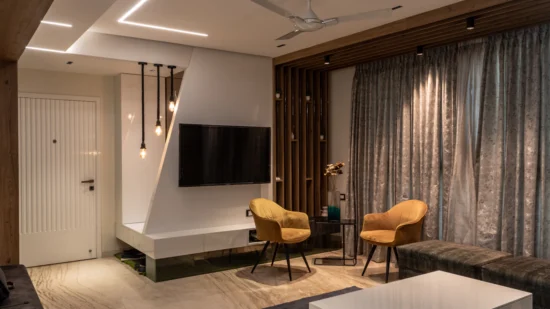 Apartment living room with a wall-mounted TV, two accent chairs, full-height curtains and a false ceiling with profile lights