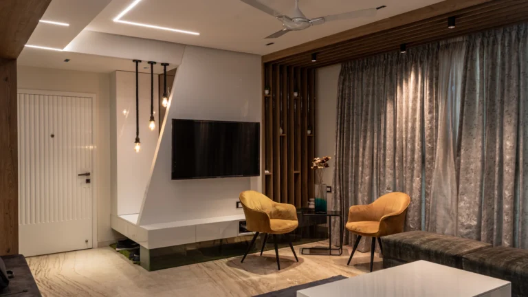 Apartment living room with a wall-mounted TV, two accent chairs, full-height curtains and a false ceiling with profile lights