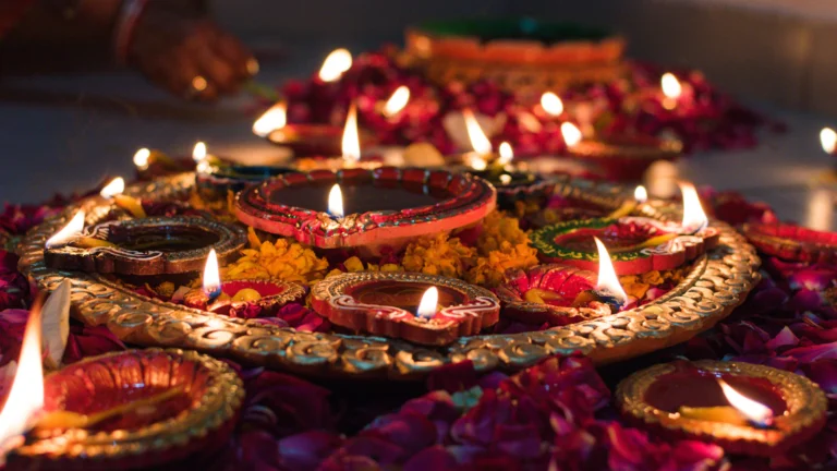 Lit clay diyas on a decorative tray surrounded by flower petals